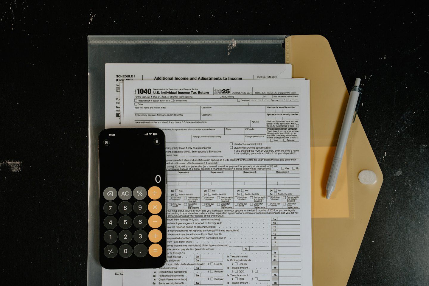 Formularios de impuestos con una calculadora de smartphone y un bolígrafo sobre un escritorio oscuro.