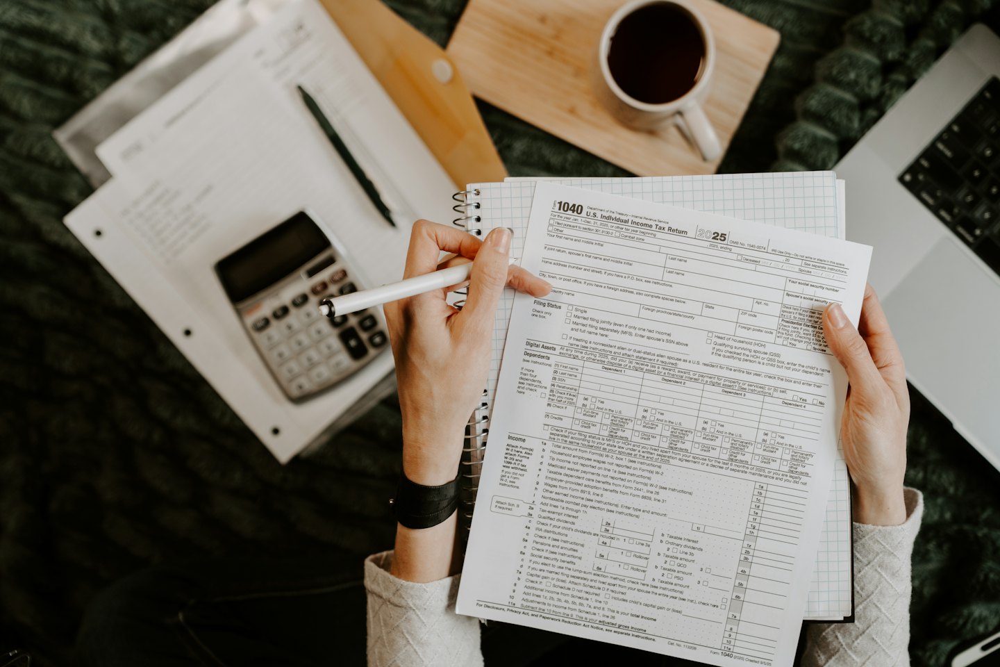 Manos revisando un formulario de impuestos con bolígrafo, portátil y calculadora.